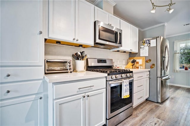 kitchen with ornamental molding, white cabinets, stainless steel appliances, light hardwood / wood-style floors, and backsplash