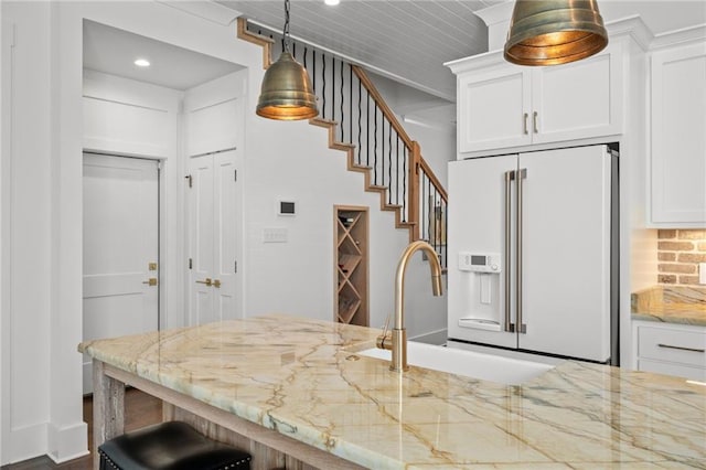 kitchen featuring high end fridge, a sink, white cabinetry, light stone countertops, and hanging light fixtures