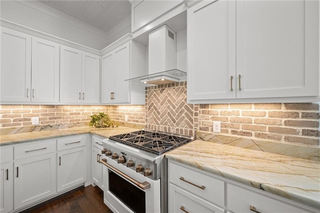 kitchen featuring light stone counters, range with gas stovetop, white cabinetry, wall chimney range hood, and decorative backsplash