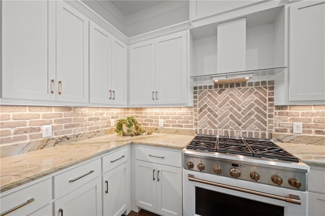 kitchen with wall chimney range hood, light stone counters, range with gas stovetop, decorative backsplash, and white cabinetry