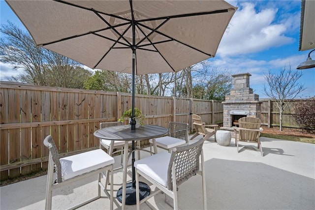 view of patio featuring outdoor dining space, an outdoor stone fireplace, and a fenced backyard