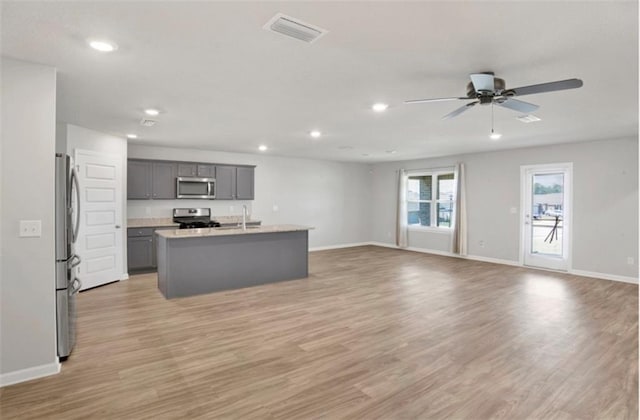 kitchen with visible vents, appliances with stainless steel finishes, open floor plan, a kitchen island with sink, and light countertops