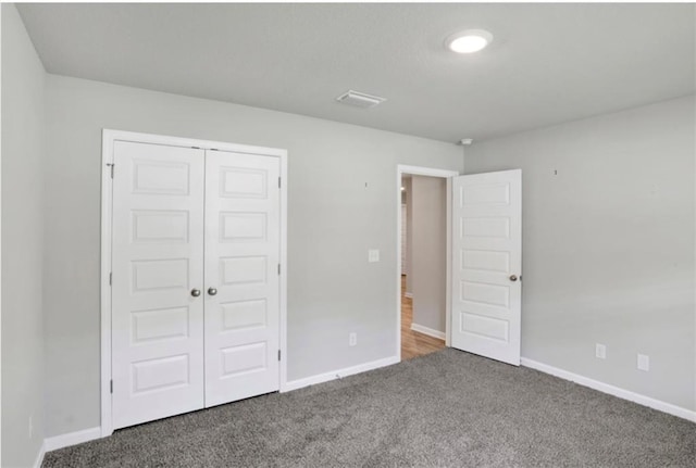 unfurnished bedroom with visible vents, baseboards, dark colored carpet, and a closet