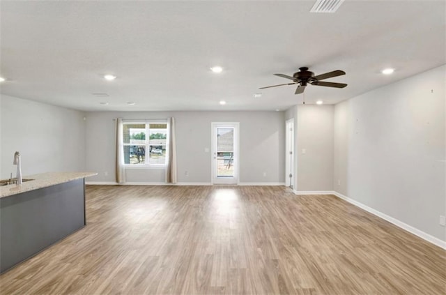 unfurnished living room featuring light wood-style flooring, baseboards, a sink, and recessed lighting