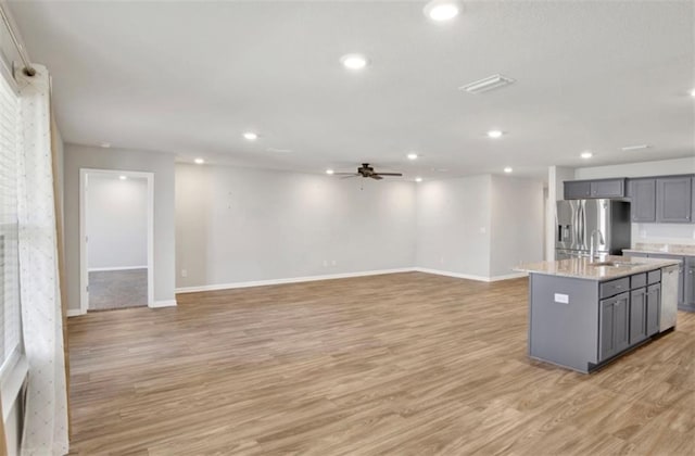 kitchen featuring open floor plan, stainless steel appliances, gray cabinets, and a center island with sink