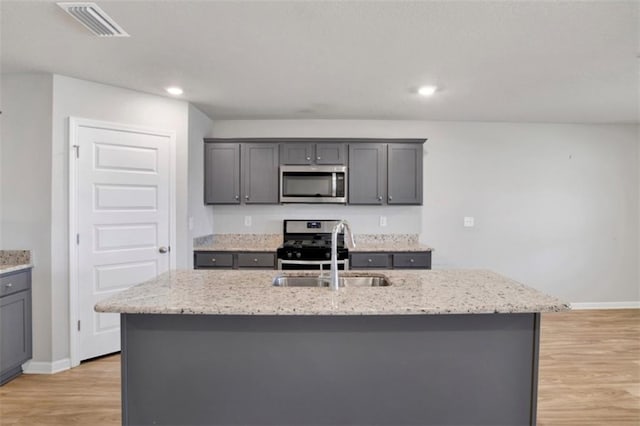 kitchen featuring gray cabinetry, a sink, visible vents, appliances with stainless steel finishes, and an island with sink