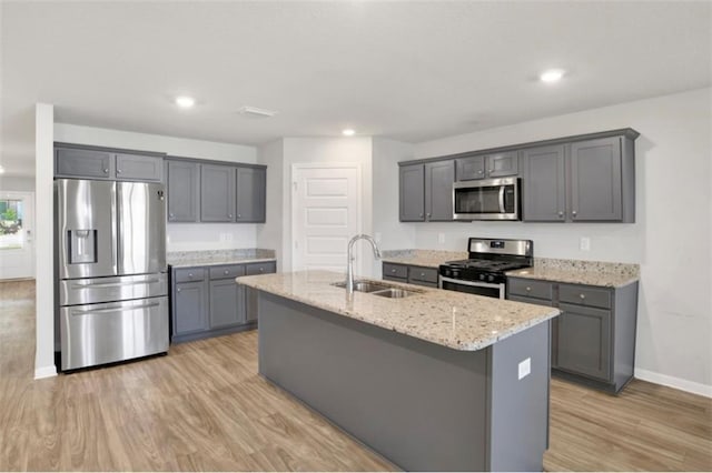 kitchen featuring light wood finished floors, stainless steel appliances, gray cabinetry, a kitchen island with sink, and a sink