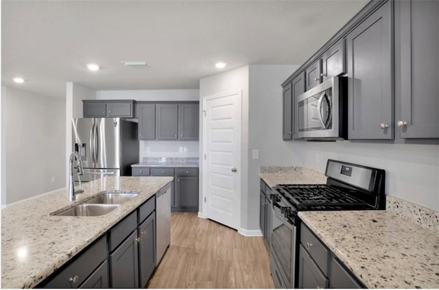 kitchen with a sink, light wood-style floors, appliances with stainless steel finishes, gray cabinets, and light stone countertops