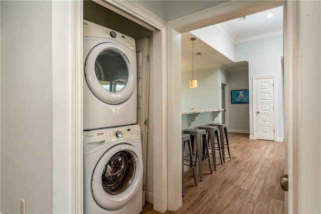 laundry area featuring laundry area, stacked washer / dryer, wood finished floors, baseboards, and crown molding