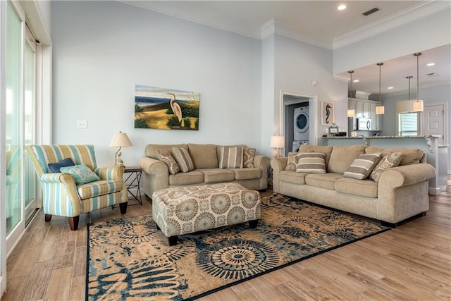 living room with stacked washer and dryer, recessed lighting, visible vents, ornamental molding, and light wood-type flooring