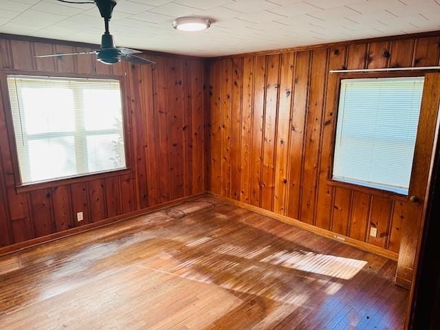 spare room with wooden walls, wood-type flooring, a ceiling fan, and baseboards