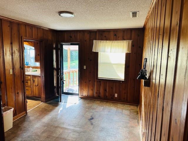 interior space featuring visible vents, wood walls, a textured ceiling, and tile patterned floors