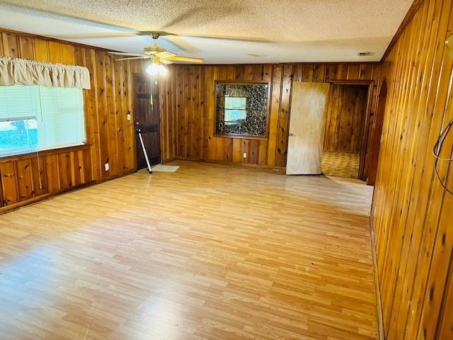 spare room with light wood finished floors, wooden walls, a ceiling fan, and a textured ceiling