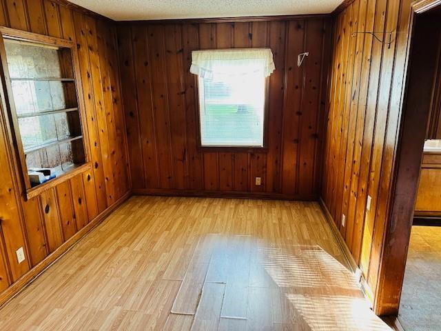 unfurnished room featuring a textured ceiling, wood walls, light wood-type flooring, and baseboards