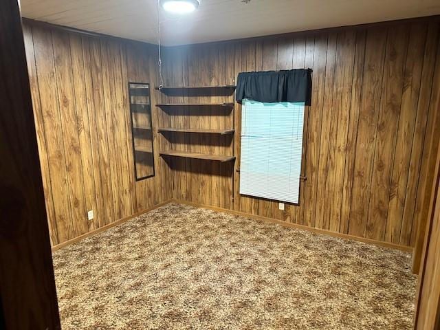 unfurnished room featuring wooden walls, baseboards, and carpet flooring