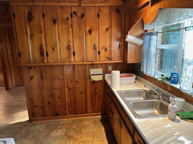 kitchen with light countertops, brown cabinetry, a sink, and wooden walls