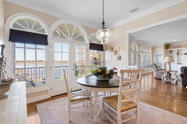 dining space with visible vents, ornamental molding, a water view, and wood finished floors
