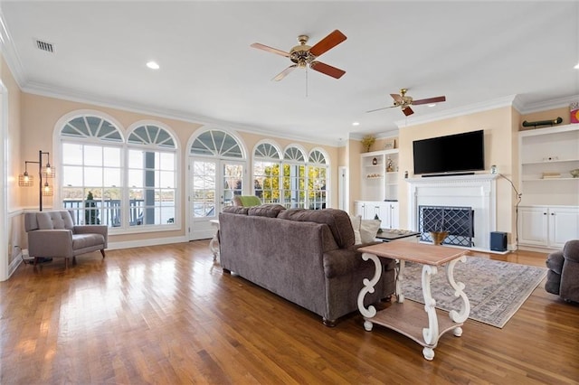 living area with visible vents, ornamental molding, wood finished floors, and a ceiling fan