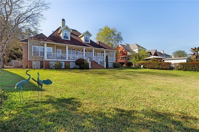 back of property featuring covered porch, a chimney, brick siding, and a yard