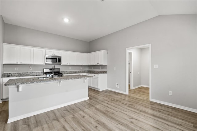 kitchen with sink, an island with sink, light stone counters, white cabinetry, and stainless steel appliances