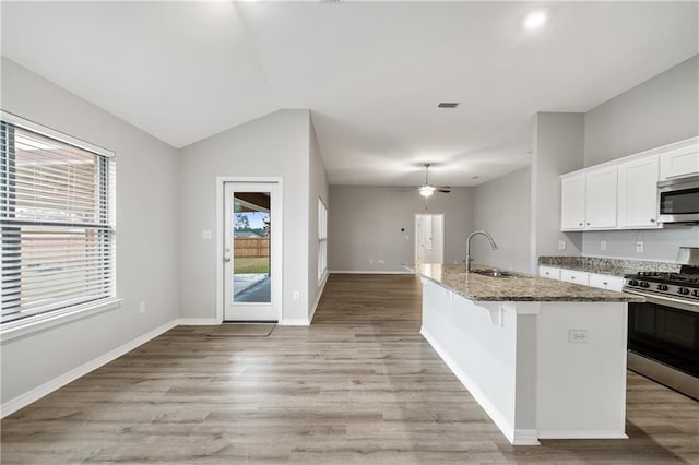 kitchen featuring a center island with sink, sink, dark stone countertops, appliances with stainless steel finishes, and white cabinetry