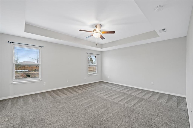 empty room with ceiling fan, carpet floors, and a tray ceiling