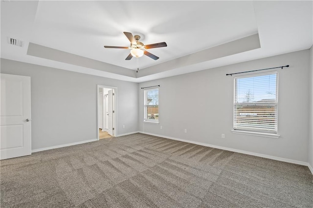 empty room with light colored carpet, a raised ceiling, and ceiling fan