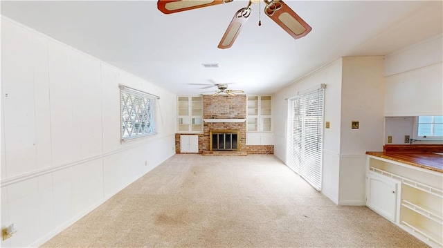 unfurnished living room featuring ceiling fan, light colored carpet, visible vents, built in features, and a brick fireplace