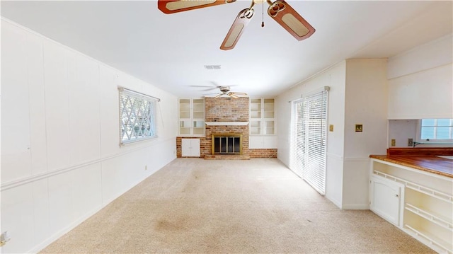 unfurnished living room with light colored carpet, a fireplace, visible vents, built in features, and a ceiling fan