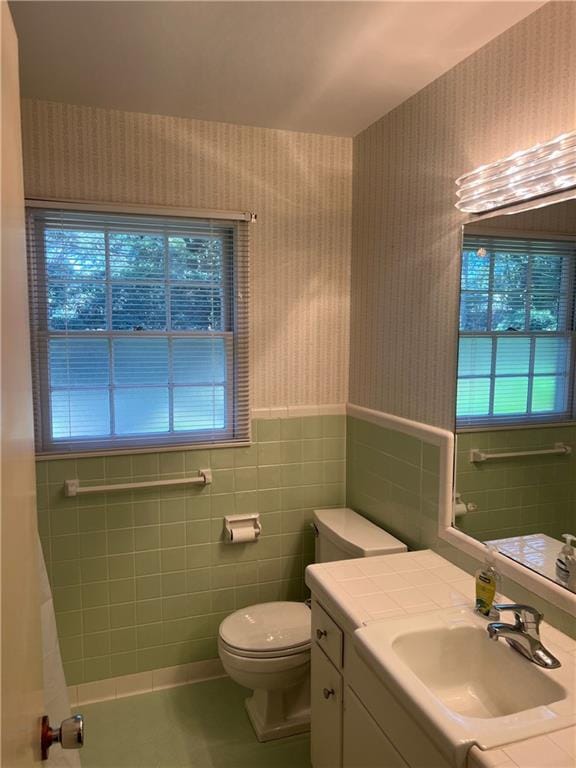 full bath with wallpapered walls, toilet, tile patterned floors, vanity, and tile walls