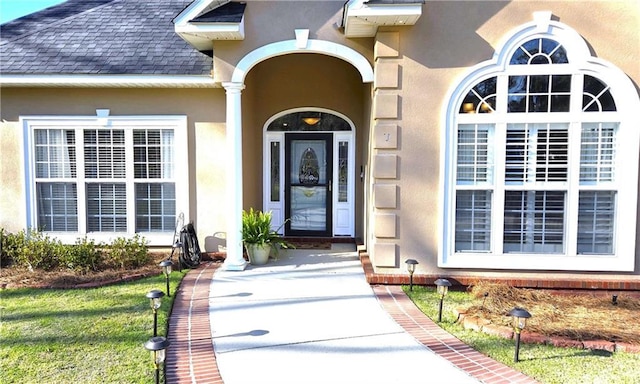 doorway to property featuring stucco siding and roof with shingles