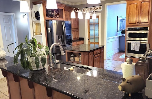 kitchen with a wainscoted wall, dark stone counters, a sink, stainless steel appliances, and a center island