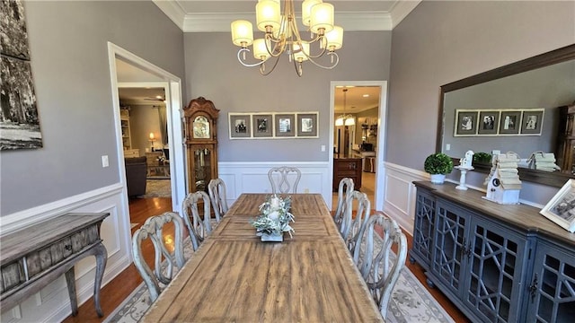 dining space with a wainscoted wall, a notable chandelier, wood finished floors, and crown molding