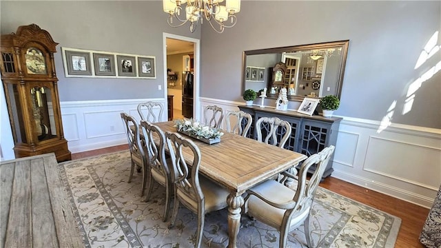 dining space featuring a wainscoted wall, wood finished floors, and a chandelier