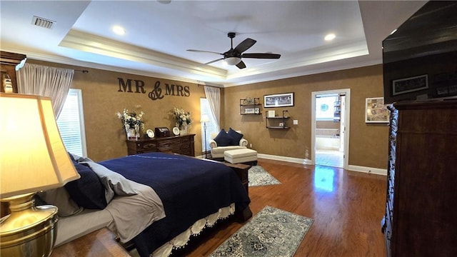 bedroom with a tray ceiling, crown molding, wood finished floors, and visible vents