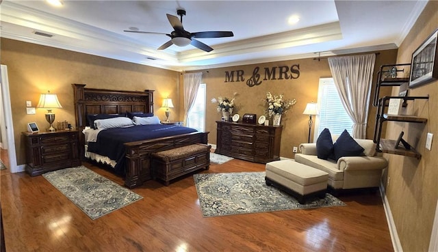 bedroom with visible vents, crown molding, baseboards, a tray ceiling, and wood finished floors