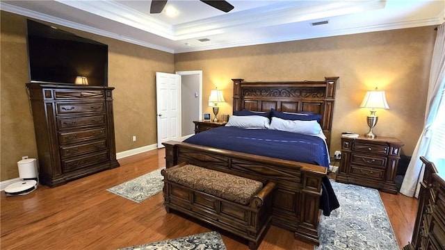 bedroom featuring visible vents, wood finished floors, baseboards, crown molding, and a raised ceiling