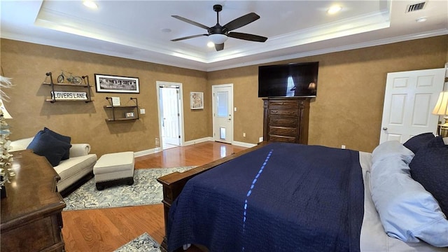 bedroom with visible vents, a raised ceiling, wood finished floors, and ornamental molding