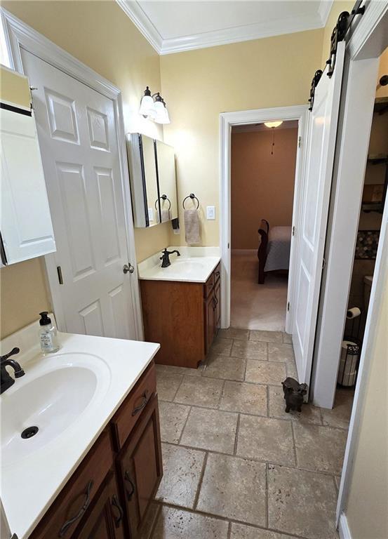 bathroom featuring a sink, stone tile floors, two vanities, and ornamental molding