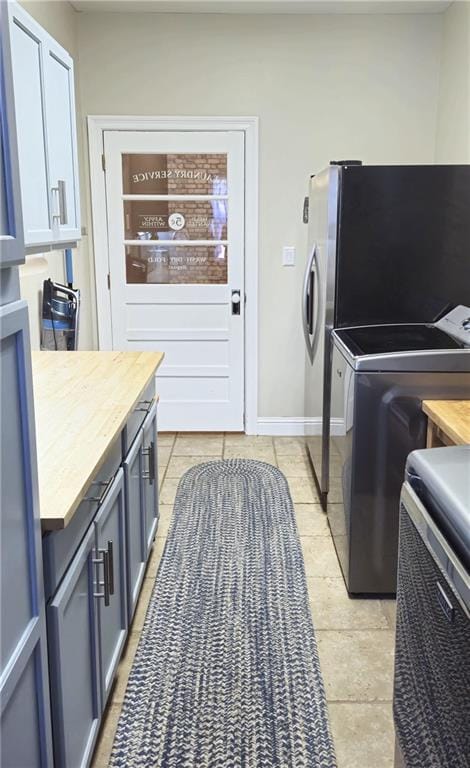 laundry room featuring washer and dryer, light tile patterned floors, cabinet space, and baseboards