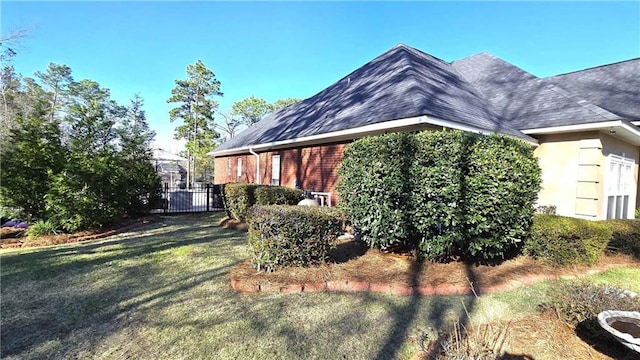 view of side of property featuring brick siding, a lawn, a shingled roof, and fence