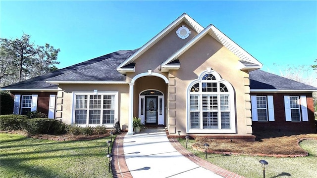 view of front facade with a shingled roof, a front yard, and stucco siding