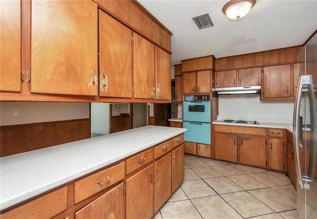 kitchen featuring visible vents, brown cabinetry, light countertops, under cabinet range hood, and double oven