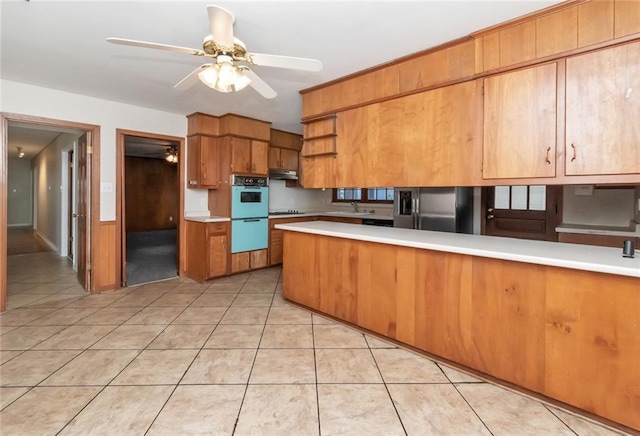 kitchen with a peninsula, multiple ovens, light countertops, freestanding refrigerator, and brown cabinetry