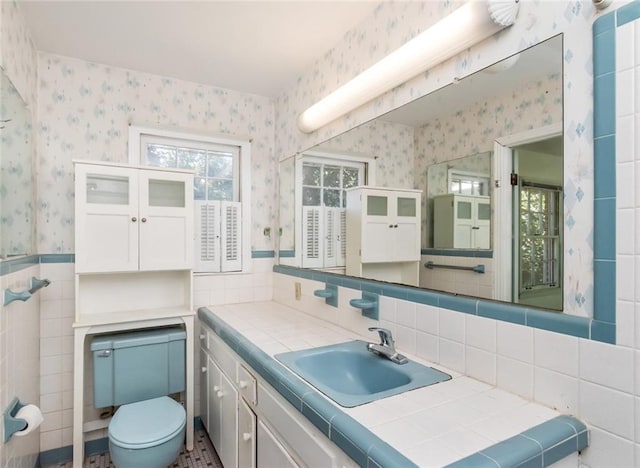 bathroom with a wainscoted wall, tile walls, toilet, vanity, and wallpapered walls