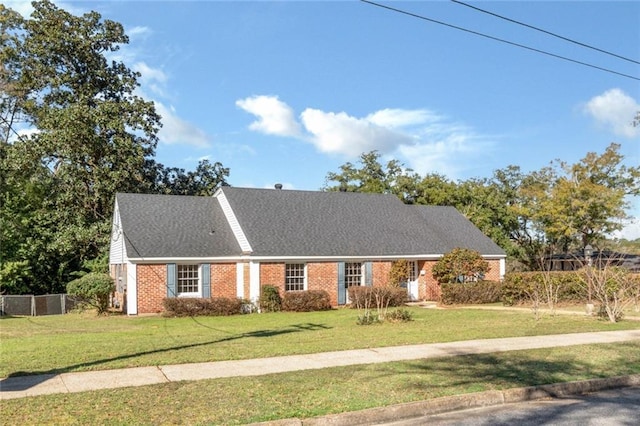 view of front of property with a front yard, brick siding, fence, and roof with shingles