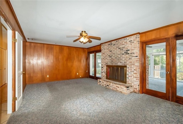 unfurnished living room featuring wooden walls, a fireplace, crown molding, and carpet flooring