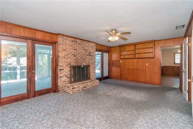 unfurnished living room with carpet floors, crown molding, a fireplace, visible vents, and wooden walls