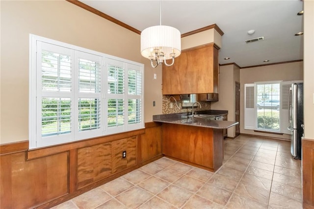 kitchen featuring pendant lighting, kitchen peninsula, stainless steel refrigerator, decorative backsplash, and ornamental molding