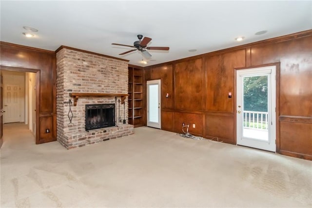 unfurnished living room featuring a fireplace, wooden walls, ceiling fan, and light colored carpet